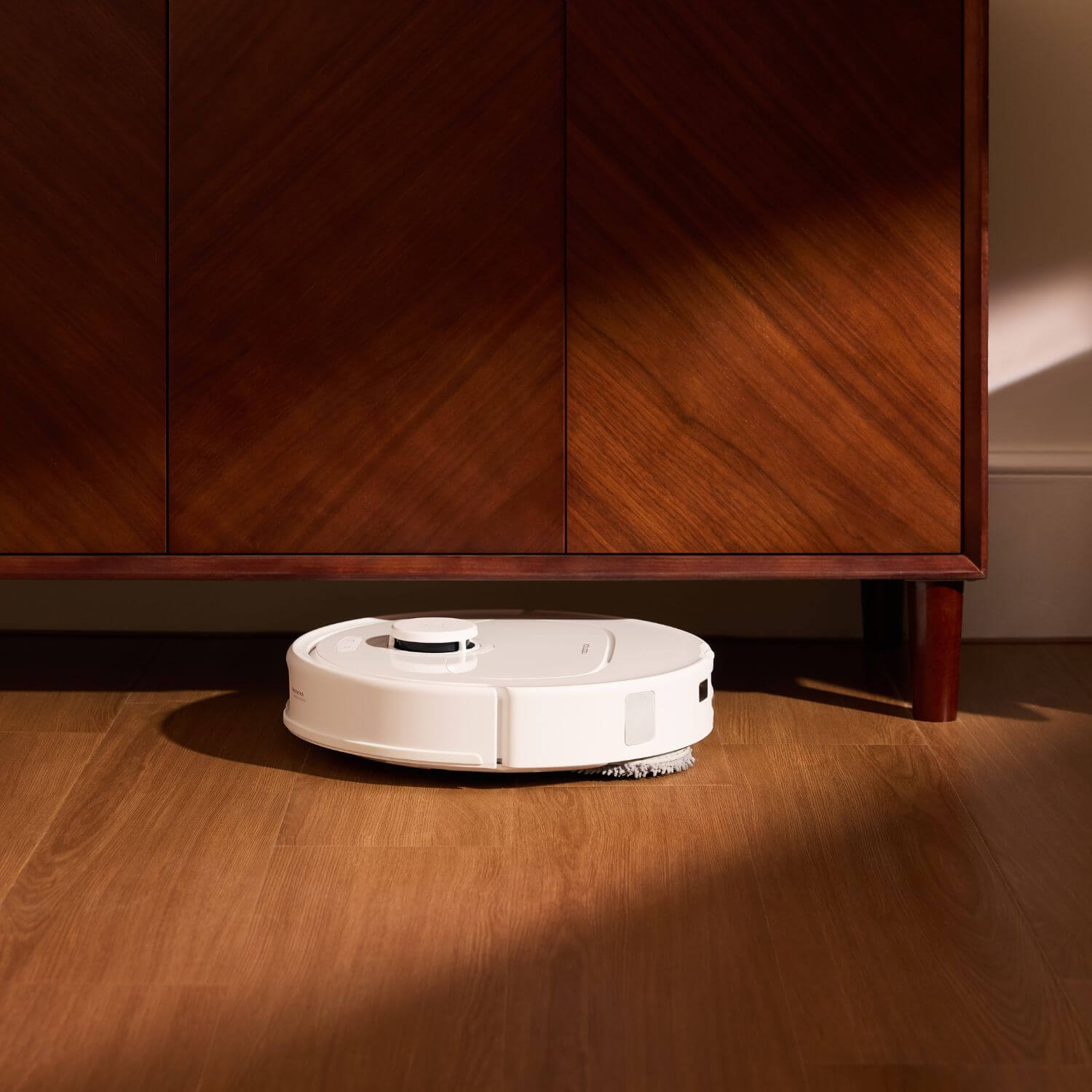 Roborock QR 798 robotti-imuri ja -moppi siivoamassa puulattialla kaapin alla.